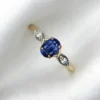 Macro photograph of a 1.91-gram 18K yellow gold fine ring set with a central 0.68-carat vibrant royal blue Ceylon sapphire flanked by sparkling diamond accents (0.04 CTW) on marquise-style shoulder settings against a white background.